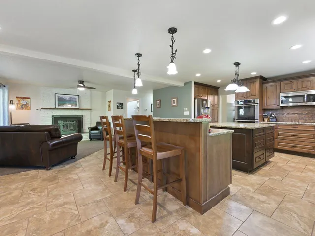 a kitchen with stainless steel appliances kitchen island granite countertop a refrigerator a stove top oven and a sink with dining table