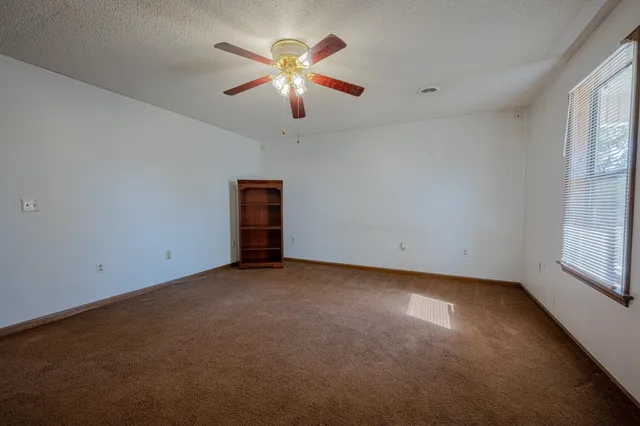 an empty room with chandelier fan and windows