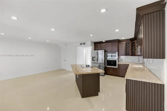 a kitchen with stainless steel appliances kitchen island granite countertop a refrigerator a stove and a sink with wooden cabinets