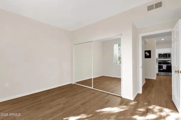 an empty room with wooden floor and way to kitchen