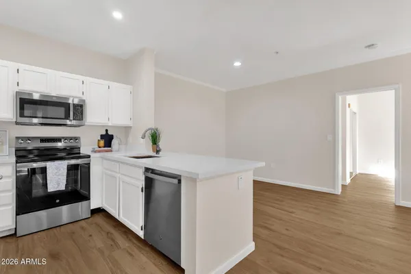 a kitchen with stainless steel appliances a stove top oven a sink a refrigerator white cabinets and wooden floor