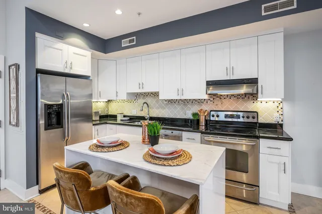 a kitchen with stainless steel appliances granite countertop a stove a sink a refrigerator and white cabinets