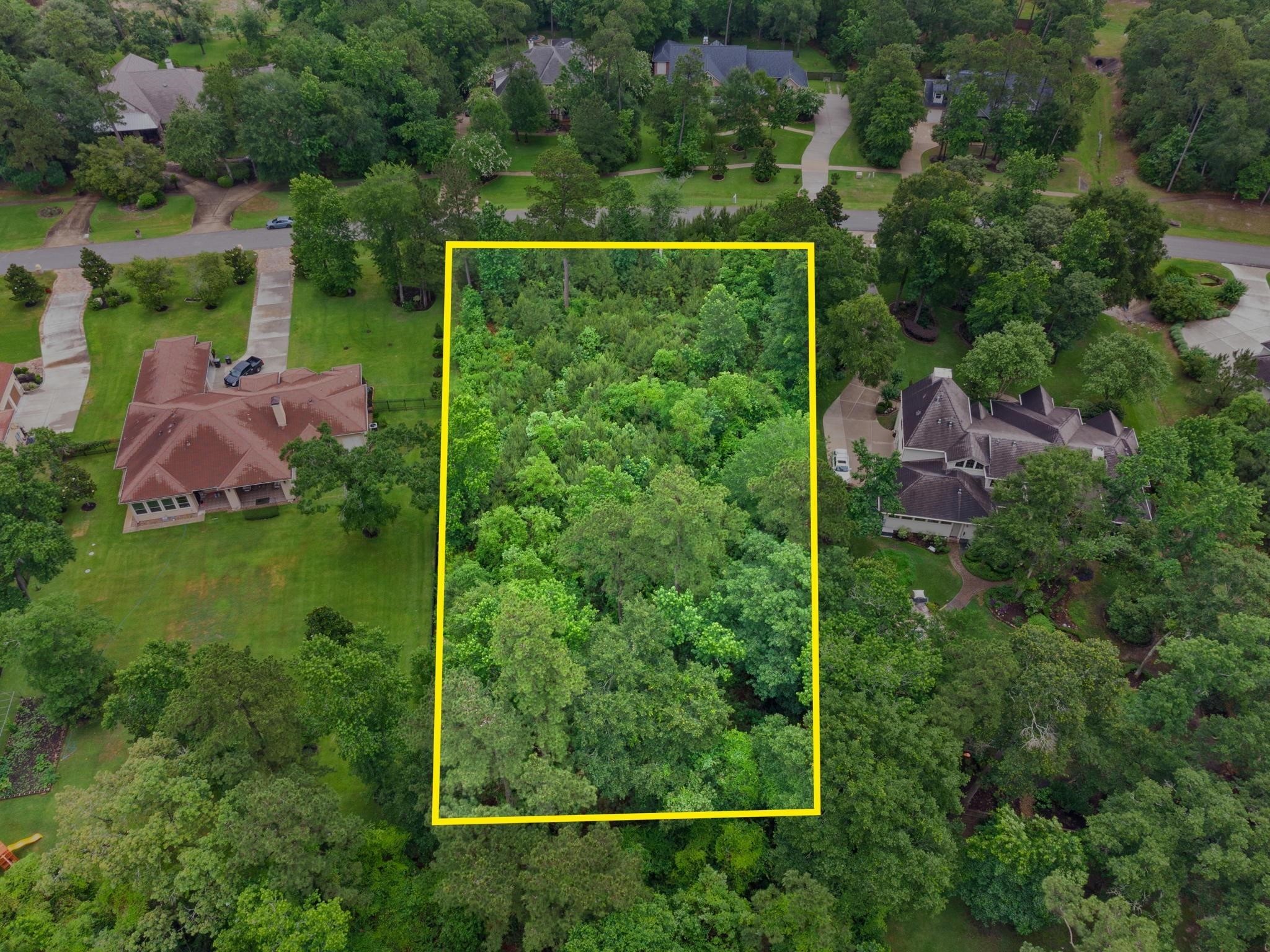 This aerial photo shows a spacious, wooded lot outlined in yellow, nestled between two elegant homes in a lush, green neighborhood. Ideal for privacy and nature lovers.