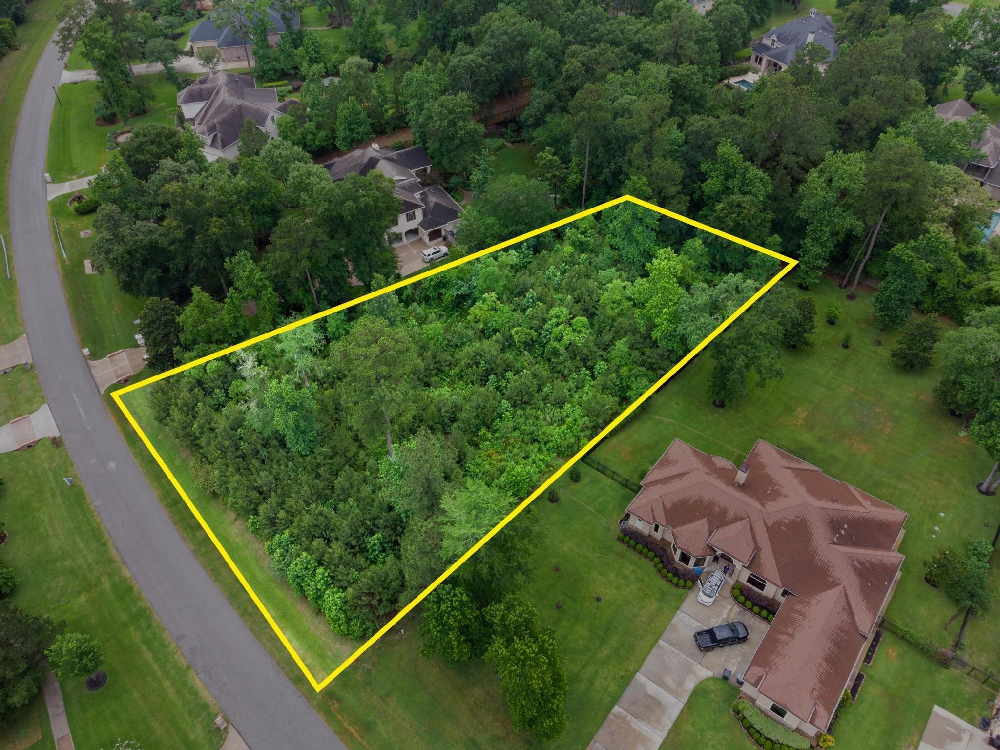 27403 Whispering Maple Way Spring, TX 77386 - Photo 4 of 10 This photo shows a spacious, wooded residential lot outlined in yellow, situated in a quiet neighborhood with nearby homes. The area is lush with greenery, offering privacy and potential for development.
