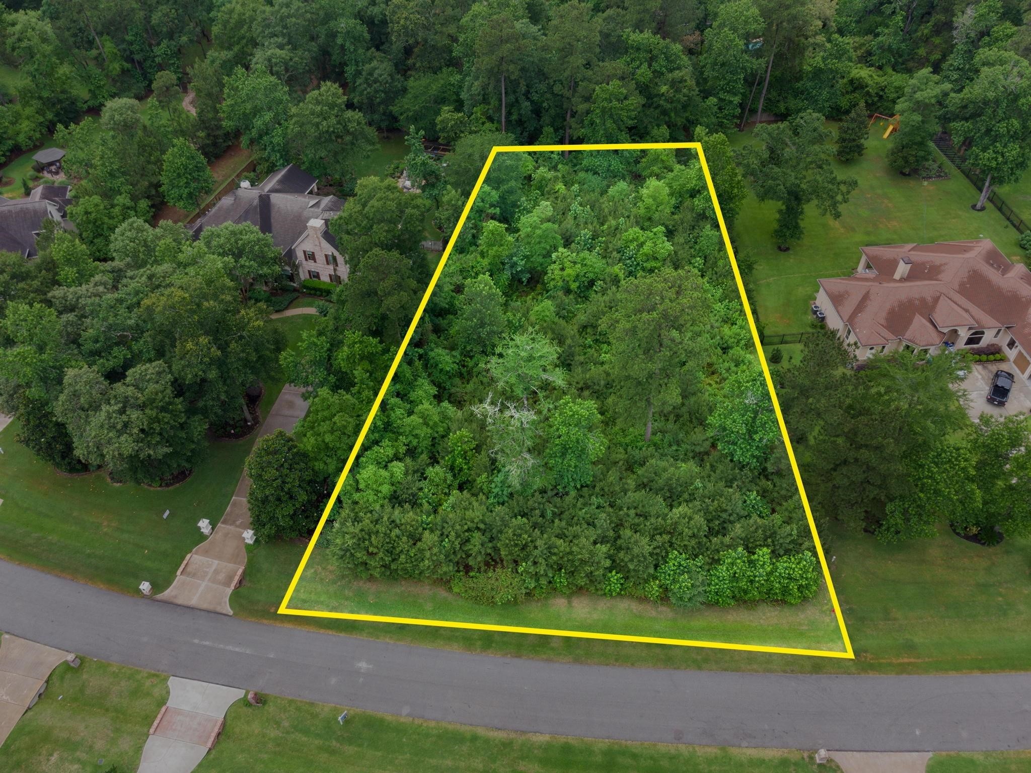 27403 Whispering Maple Way Spring, TX 77386 - Photo 9 of 10 This photo shows a spacious residential lot outlined in yellow, surrounded by lush trees and greenery. The lot is situated in a quiet, upscale neighborhood with neighboring homes nearby, offering a serene and private setting.