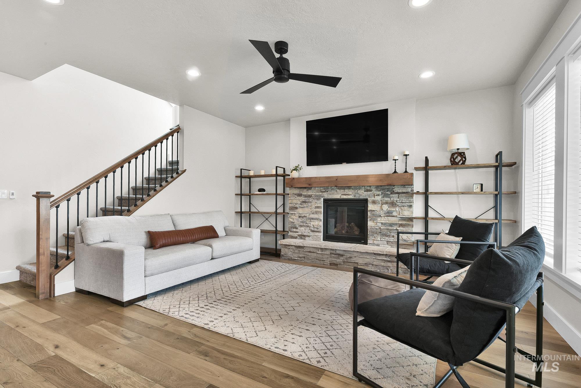 5676 East Zaffre Ridge Street Boise, ID 83716 - Photo 20 of 50 Living area featuring a stone-clad fireplace with a wood mantel, rich wood-finish flooring, a staircase with wood newel posts and metal balusters, recessed lighting, and a ceiling fan