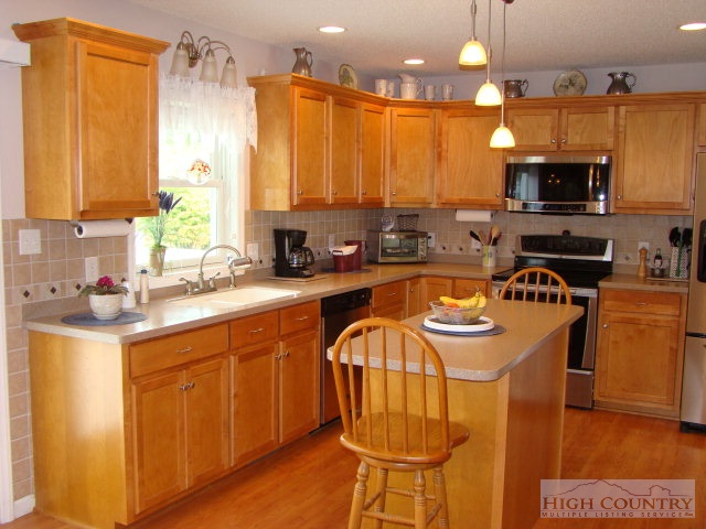 124 Alex Wellborn Road Deep Gap, NC 28618 - Photo 3 of 26 a kitchen with stainless steel appliances a sink a stove a refrigerator cabinets and a dining table with wooden floor