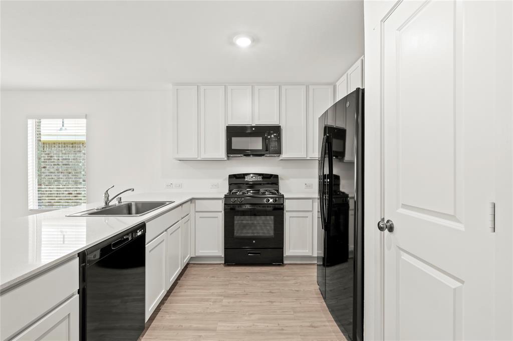 1138 Barbary Flds Street Forney, TX 75126 - Photo 10 of 25 Kitchen featuring white cabinetry, black appliances, a double basin sink, light-toned wood-finish flooring, and white countertops
