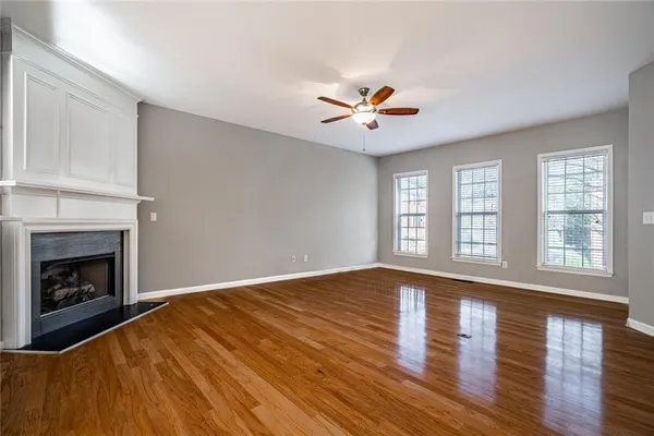 a view of an empty room with wooden floor fireplace and a window