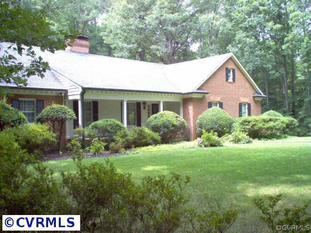 a house that is sitting in the grass with large trees and plants