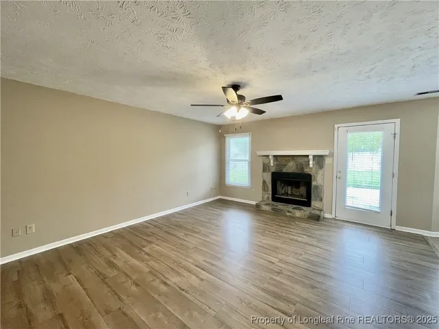 an empty room with wooden floor fireplace and windows