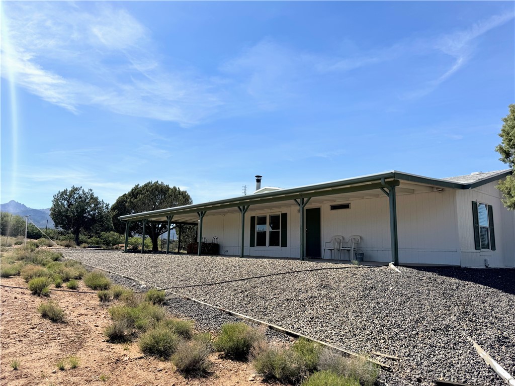 The property features a long covered porch, a gravel pathway leading to the entrance, and a white exterior with dark green trim