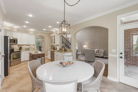 a kitchen with stainless steel appliances kitchen island granite countertop a dining table chairs and a refrigerator