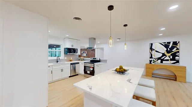 a large white kitchen with stainless steel appliances granite countertop a sink dishwasher a stove and a dining table with wooden floor