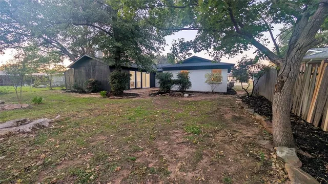 a backyard of a house with plants and large tree