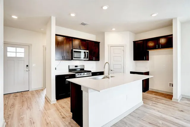 a kitchen with stainless steel appliances a stove top oven a sink a refrigerator white cabinets and wooden floor