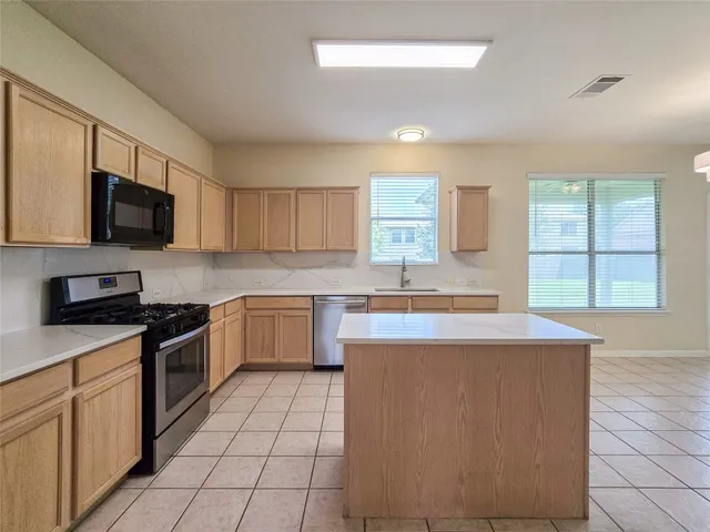 a kitchen with kitchen island granite countertop a stove top oven a sink a counter top space and cabinets