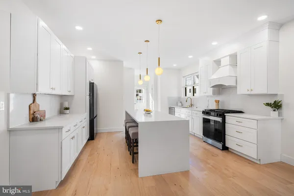 a large kitchen with stainless steel appliances kitchen island granite countertop a stove a sink a refrigerator and white cabinets with wooden floor
