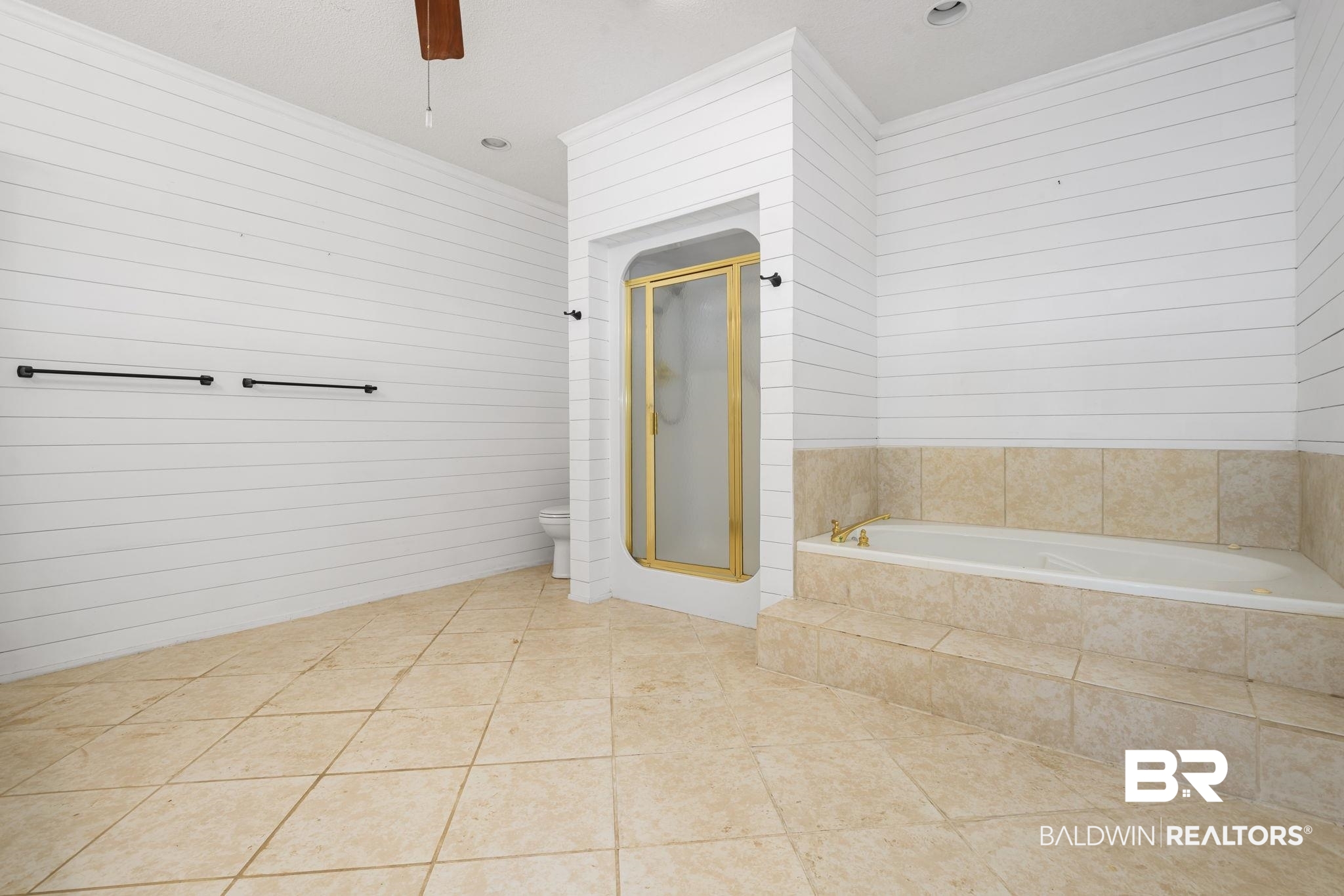 7540 2 Mile Road Irvington, AL 36544 - Photo 33 of 82 Spacious bathroom featuring neutral-toned tile flooring, a built-in soaking tub with tiled surround, a separate shower enclosure with gold-toned framing, and white shiplap walls