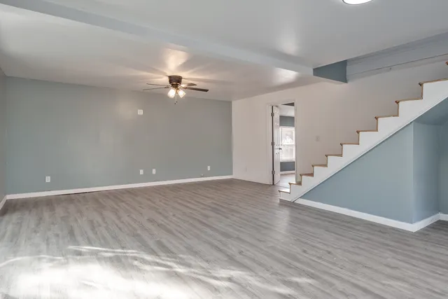 a view of an empty room with wooden floor and a ceiling fan