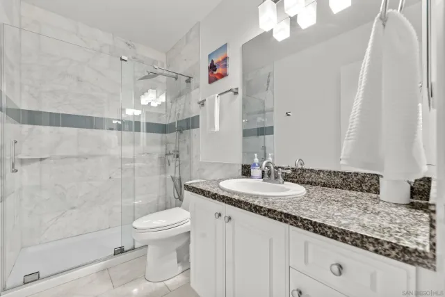 a bathroom with a granite countertop sink a toilet a mirror and shower