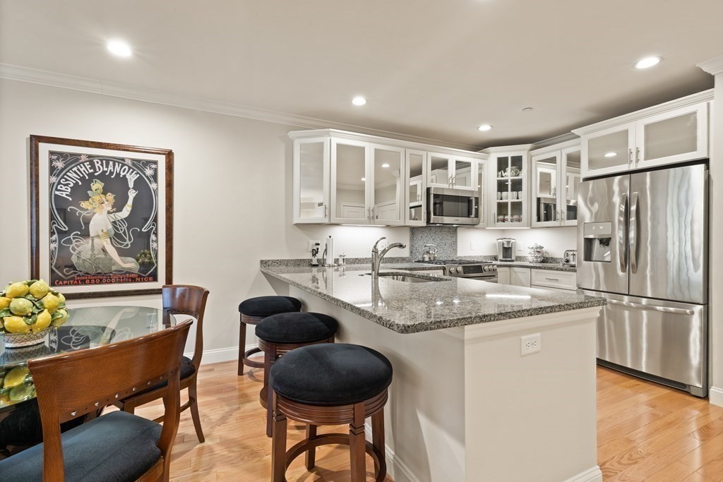 2 Manor Terrace, Unit 209 Lexington, MA 02420 - Photo 11 of 26 a kitchen with stainless steel appliances granite countertop a refrigerator a sink a stove a dining table and chairs with wooden floor