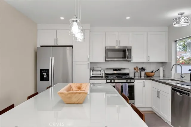 a kitchen with stainless steel appliances kitchen island granite countertop a refrigerator a sink a stove and white cabinets