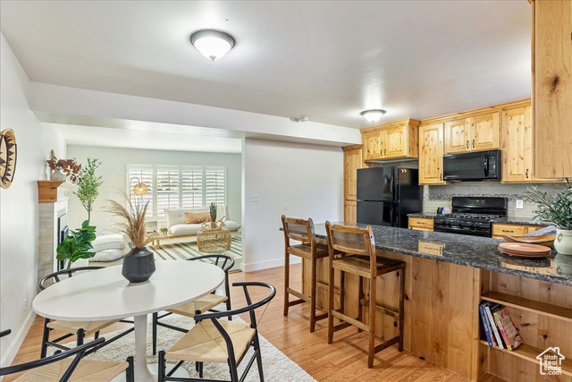 2260 East Murray Holladay Road, Unit 32 Holladay, UT 84117 - Photo 1 of 1 Kitchen featuring black appliances, a breakfast bar, dark stone counters, light wood finished floors, and decorative backsplash