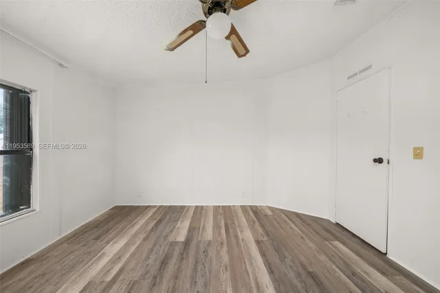 a view of a room with wooden floor ceiling fan and window