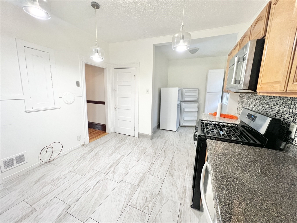 18 Sherman Street, Unit 1 Everett, MA 02149 - Photo 7 of 11 a kitchen with stainless steel appliances granite countertop a refrigerator oven stove a sink and a dining table with wooden floor