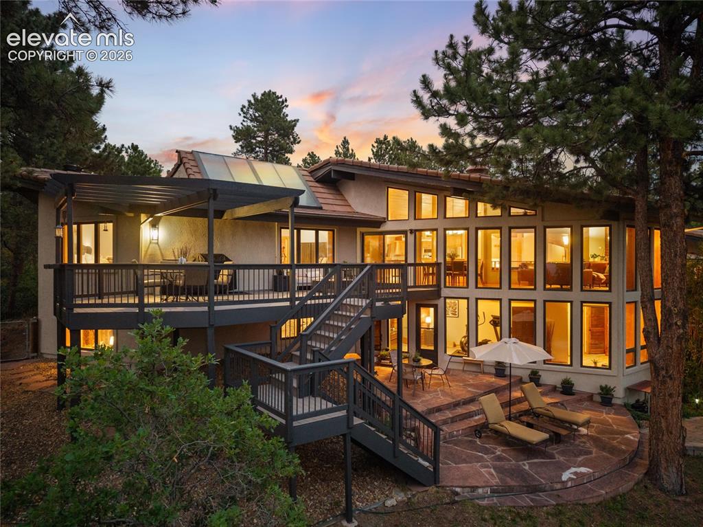 12730 Bridle Bit Road Colorado Springs, CO 80908 - Photo 45 of 50 Multi-level rear exterior featuring a large upper deck with a pergola, a curved flagstone patio, and extensive window walls