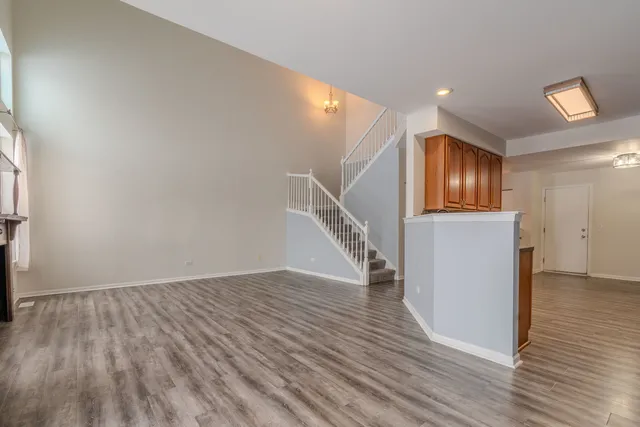 a view of an empty room with wooden floor and a kitchen