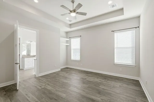an empty room with wooden floor ceiling fan and windows