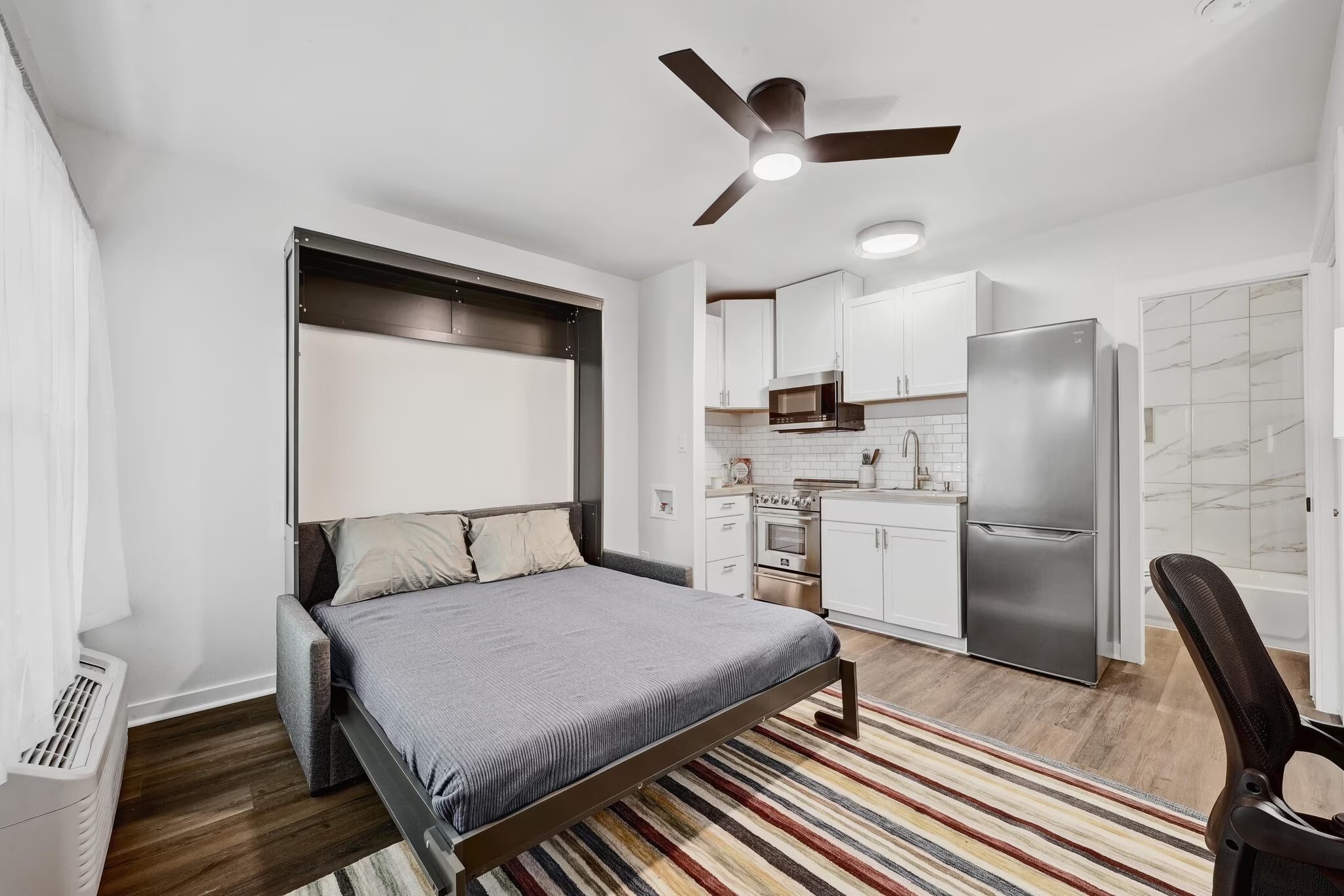 2802 Whitis Avenue, Unit 106 Austin, TX 78705 - Photo 2 of 8 Compact living space featuring a wall-mounted bed system, wood-finish flooring, and a ceiling fan