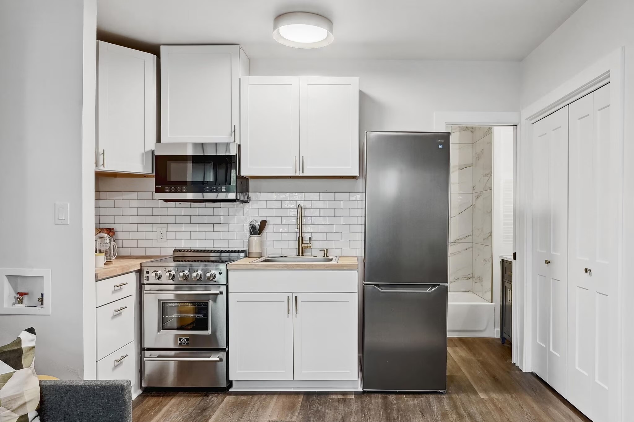 2802 Whitis Avenue, Unit 106 Austin, TX 78705 - Photo 5 of 8 Compact kitchen featuring white flat-panel cabinetry, stainless steel appliances, wood-finish countertops, subway tile backsplash, and wood-finish flooring