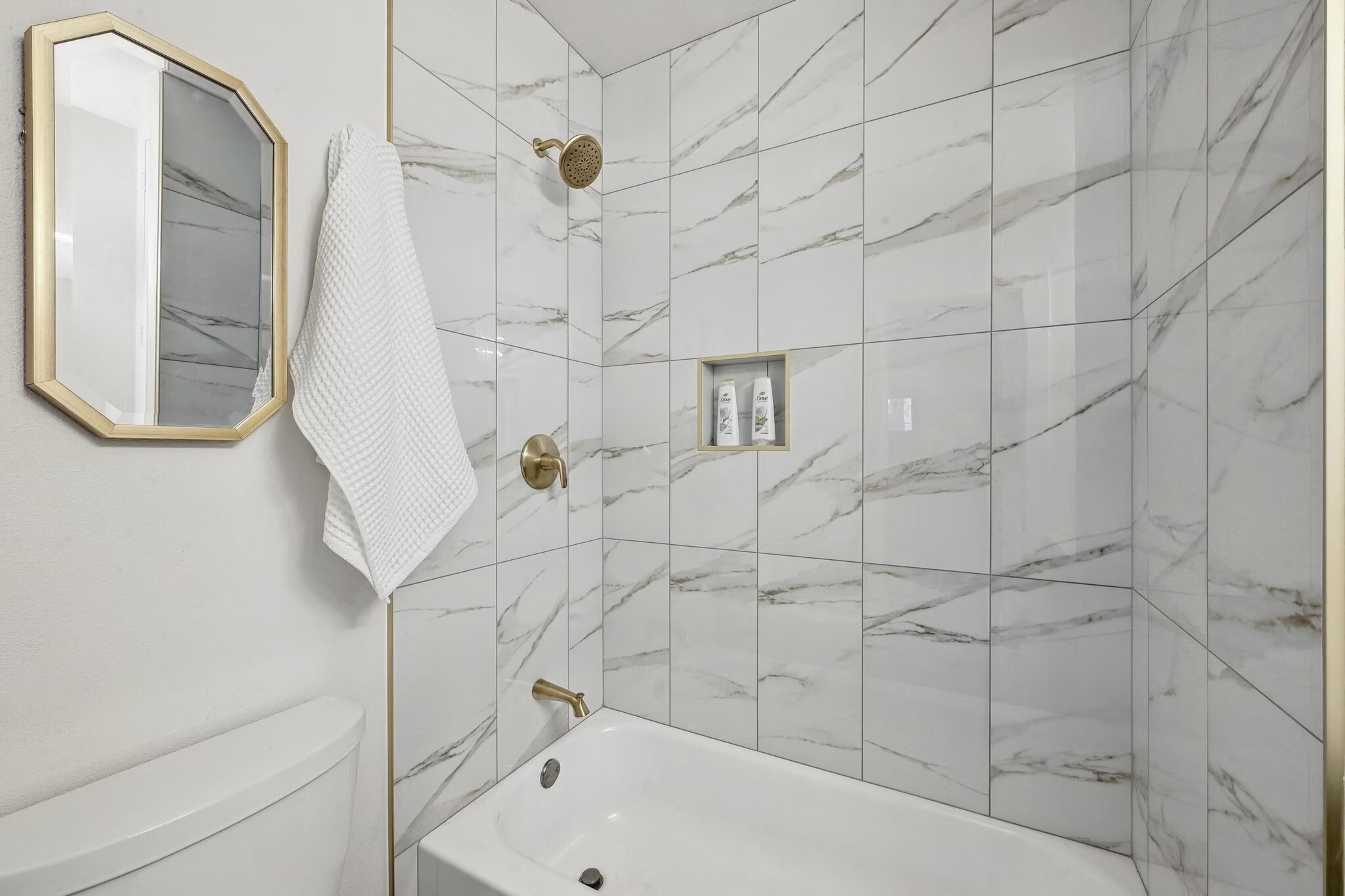 2802 Whitis Avenue, Unit 106 Austin, TX 78705 - Photo 7 of 8 Bathtub and shower combination featuring white marble-look subway tile surrounds, brass fixtures, and a recessed shower niche