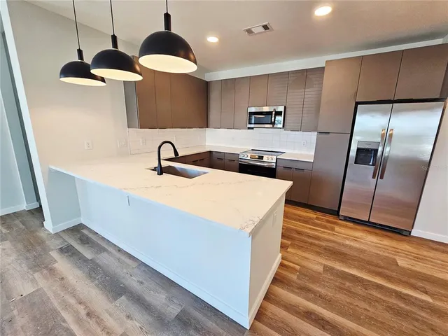 a kitchen with stainless steel appliances granite countertop a sink a refrigerator and a wooden floor