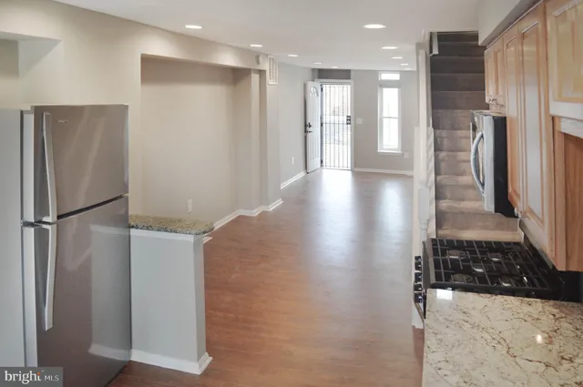 a view of a refrigerator in kitchen and an empty room with wooden floor