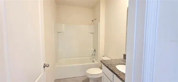 a bathroom with a granite countertop bathtub shower sink mirror vanity and toilet