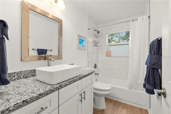 a bathroom with a granite countertop sink a toilet a mirror and shower