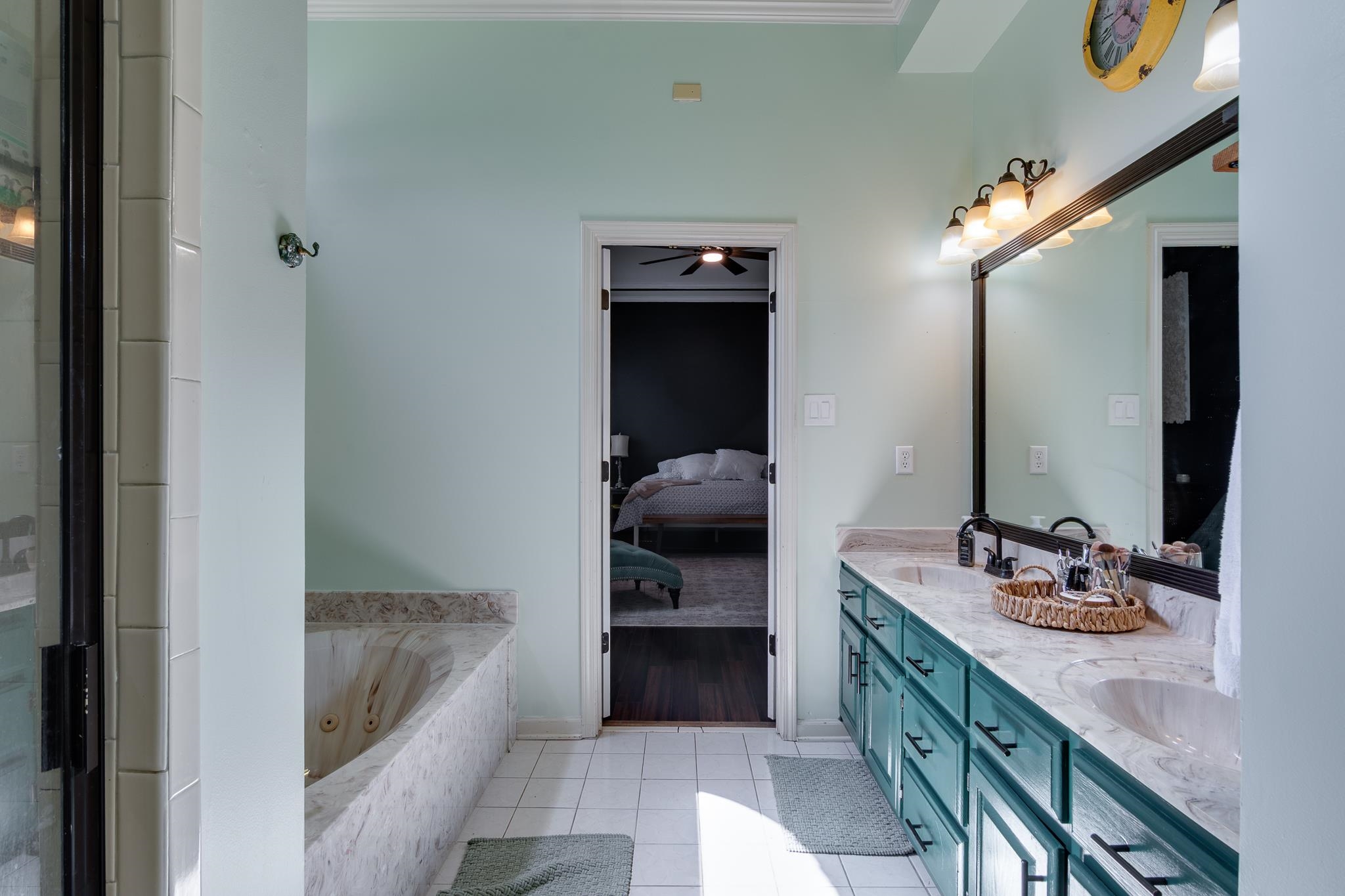 779 Early Earner Cove Collierville, TN 38017 - Photo 16 of 29 Bathroom featuring a dual vanity with a light-colored countertop and teal cabinetry, a large mirror with integrated lighting, a built-in tub with stone-look surround, and white tile flooring