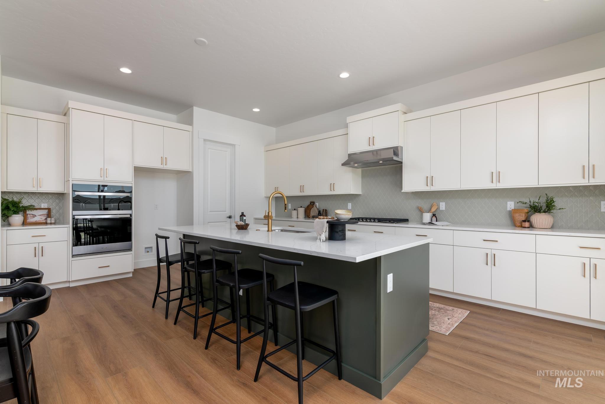 14703 Serenity Pt Street Caldwell, ID 83607 - Photo 11 of 45 Contemporary kitchen featuring a dark green island with countertop seating, white perimeter cabinetry, and wood-finish flooring