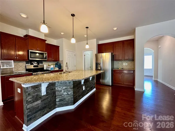 a large kitchen with stainless steel appliances kitchen island granite countertop a stove a refrigerator a oven and a wooden cabinets