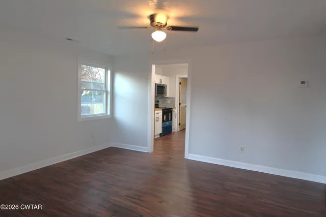 an empty room with wooden floor chandelier fan and windows