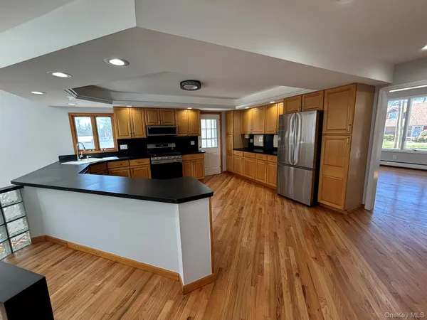 a kitchen with stainless steel appliances granite countertop a refrigerator a sink dishwasher a stove and white countertops with wooden floor