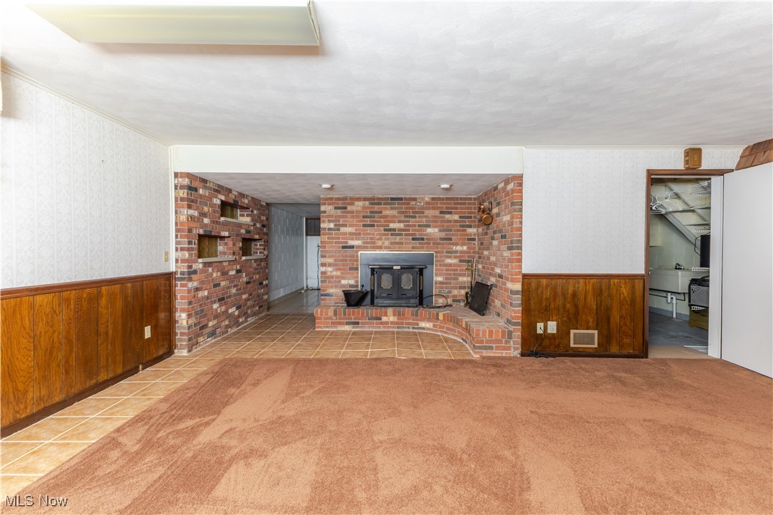 155 Forest Road Weirton, WV 26062 - Photo 20 of 28 Unfurnished living room with wainscoting, wood walls, wallpapered walls, tile patterned flooring, and a wood stove