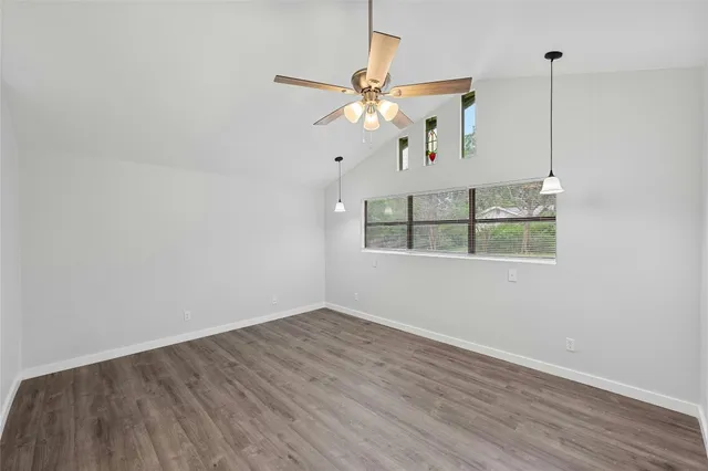 a view of an empty room with wooden floor and a ceiling fan
