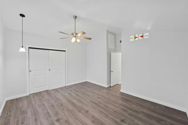 a view of an empty room with chandelier fan and wooden floor