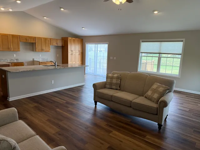 a living room with kitchen island granite countertop wooden floor a couch and a window