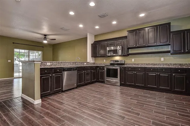 a kitchen with stainless steel appliances granite countertop wooden cabinets counter top space and wooden floor